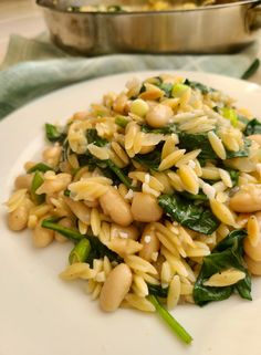 a white plate topped with pasta and greens next to a pot of broccoli