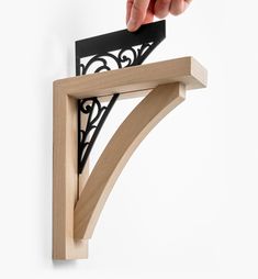 a hand holding a piece of wood on top of a wooden shelf with metal brackets