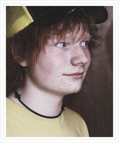 a young man with freckled hair wearing a yellow t - shirt and black hat