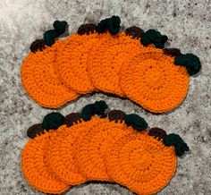 three crocheted pumpkin coasters sitting on top of a gray surface with black and brown trim