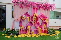 a pink and yellow display with flowers on the grass in front of a white building