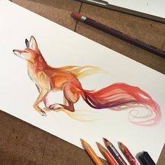 a drawing of a fox with long red hair and orange tail, on paper next to colored pencils