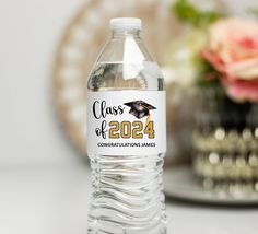 a bottle of water with a graduation cap on it sitting next to a vase filled with flowers