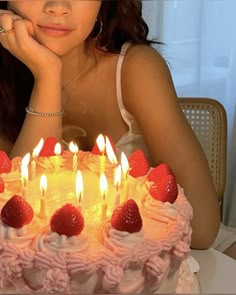 a woman sitting in front of a birthday cake with lit candles on it and strawberries