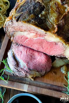 a large piece of meat sitting on top of a cutting board next to some noodles