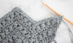 the crochet stitch is being worked on with a wooden knitting needle in front of it