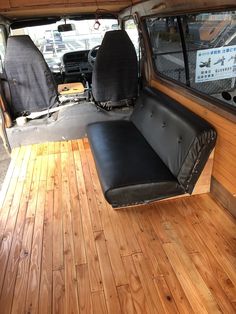 the inside of a van with wood flooring and black leather seat covers on it