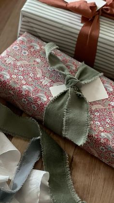 two wrapped presents sitting on top of a wooden floor next to ribbons and ribbon bows