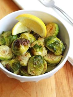 a white bowl filled with brussel sprouts and lemon wedges