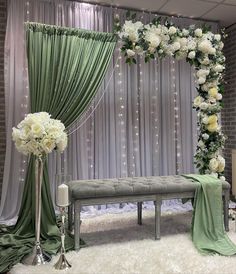 a white and green wedding ceremony setup with flowers on the altar, drapes, and bench