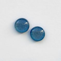 two blue glass buttons sitting on top of a white surface