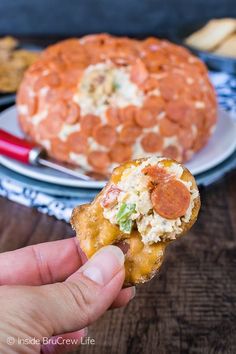 a person holding up a piece of pizza in front of a plate with crackers on it