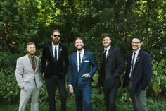 four men in suits and ties are posing for a photo outside with trees in the background