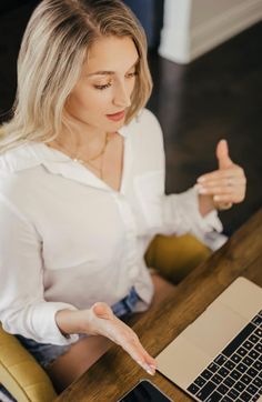 a woman sitting in front of a laptop computer giving the thumbs up sign with her hand