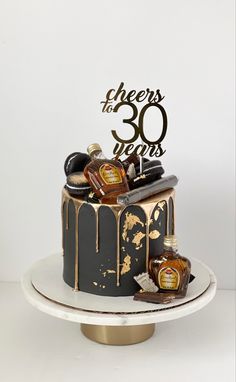 Black cake with gold drip and gold leaf details. On top and on the side there are assorted chocolates and crown royal bottles. There’s a cigar on top of the cake as well as a cake topper that reads “Cheers to 30 years”. Cake For Him Birthday, Man 30th Birthday Ideas, 30th Birthday Party For Him, Cake Black And Gold, 30th Birthday Cakes For Men, Black And Gold Birthday Cake, 35th Birthday Cakes, Cake For Him