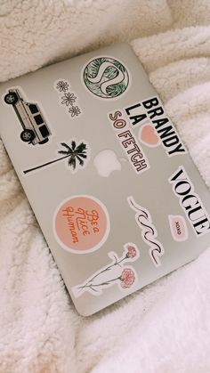 an open laptop computer sitting on top of a bed covered in white blankets and stickers