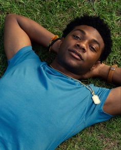 a man laying in the grass with his hand on his head and wearing a watch