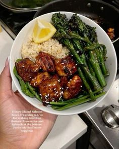 a person holding a bowl of food with broccoli and chicken on it in front of a stove