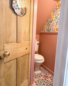 an open door leading to a bathroom with pink walls and floral wallpaper on the floor