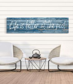 two chairs sitting next to each other in front of a wooden sign that says life is better at the beach