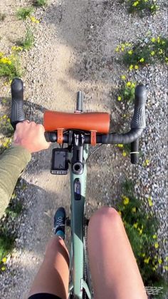 a person riding a bike down a dirt road next to grass and yellow wildflowers