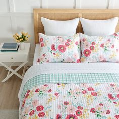 a bed with flowers on the comforter and two pillows, next to a night stand