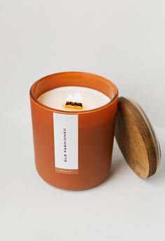 an orange candle with a wooden lid on a white surface next to a brown container