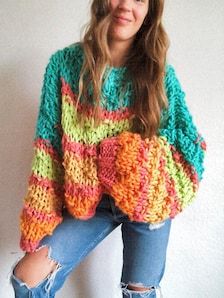 a woman wearing ripped jeans and a multicolored sweater is posing for the camera