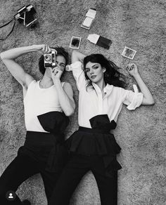 two women laying on the ground with their arms around each other, one holding a camera