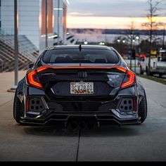 the rear end of a black sports car parked in front of a building at dusk