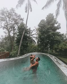 a woman sitting in the middle of a pool with palm trees around her and water falling from it