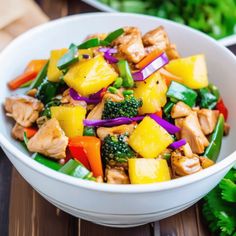 a white bowl filled with chicken, pineapples and broccoli on top of a wooden table