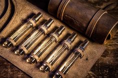 an old leather book and seven metal tubes on a wooden table with other tools in it