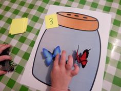 a child's hand touching a butterfly in a jar