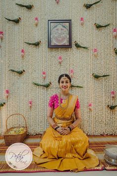 a woman sitting on the floor in front of a wall with flowers and birds hanging from it