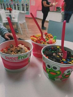 three ice cream bowls filled with different types of candy and toppings on top of a table