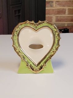 a white and green heart shaped object sitting on top of a table next to a brick wall