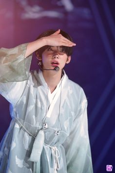 a woman in a white kimono holding her hand up to her face while standing on stage