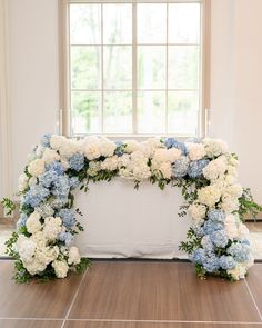 a white and blue wedding arch with flowers on the floor in front of a window