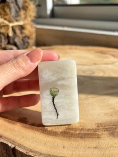 a hand holding a piece of glass with a flower painted on it's side