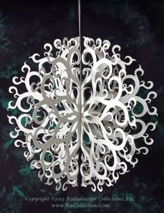 a white paper snowflake hanging from a metal hook on a black background with green and blue swirls