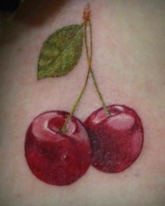 two cherries on the back of a woman's upper arm, with a green leaf