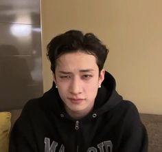 a young man sitting on top of a couch wearing a black hoodie and looking at the camera