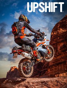 a man riding on the back of a dirt bike in the air with mountains behind him