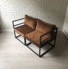 a brown couch sitting on top of a wooden floor next to a brick wall and window