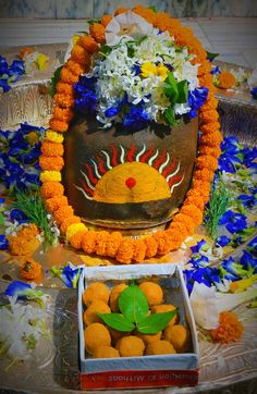 an arrangement of oranges and flowers in a vase on a table with a box of cookies