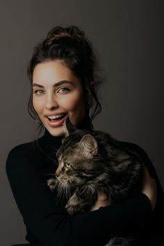 a woman holding a cat in her arms and smiling at the camera while wearing a turtle neck sweater