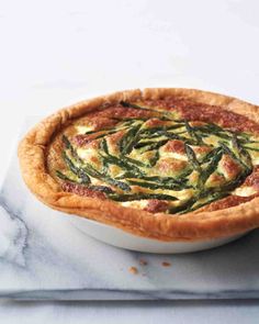 a quiche with asparagus and cheese is on a marble platter, ready to be eaten