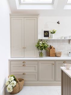 a kitchen with gray cabinets and white counter tops, flowers in vases on the shelf