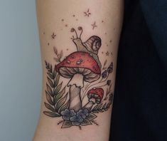 a mushroom tattoo on the arm with leaves and flowers around it, in front of a woman's right arm